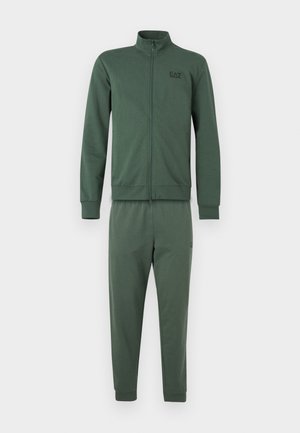 Dres z ciemnozielonego materiału, składający się z zapinanej na zamek bluzy z kołnierzem oraz dopasowanych, zwężanych spodni. Bluza ozdobiona jest małym logo.