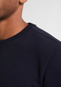 Maglione blu navy con texture a costine e motivo a diamante sul corpo; presenta un collo rotondo e cucitura spalla rinforzata.
