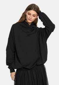 Czarny, oversize bluza z długim rękawem i luźnym dekoltem, wykonana z miękkiej bawełny. Połączona z warstwową spódnicą z czarnego tiulu.