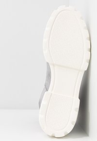 Szary zamszowy but z białą gumową podeszwą. Podeszwa ma fakturowaną, wzorzystą powierzchnię zapewniającą przyczepność i stabilność.