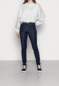 Grå oversized sweatshirt, mörkblå skinny jeans och svarta sneakers med vita sulor. Slät tyg, avslappnad passform och klassisk denimdesign.