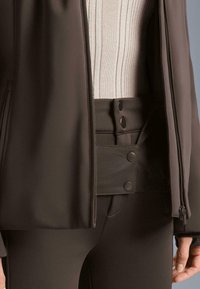 Hnedý úzky strih sako so zipsovým uzáverom, vyrobené z hladkého materiálu. Obsahuje rebrovaný krémový top pod ním a gombíkové akcenty.