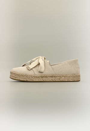 Espadrille beige en toile avec semelle épaisse en jute tressée et nœud en tissu noué sur le dessus, vue de côté sur fond neutre.