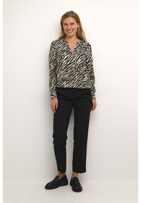 Zwart en beige blouse met lange mouwen met een zebra- en luipaardprint, gecombineerd met zwarte tapered broek en zwarte loafers.