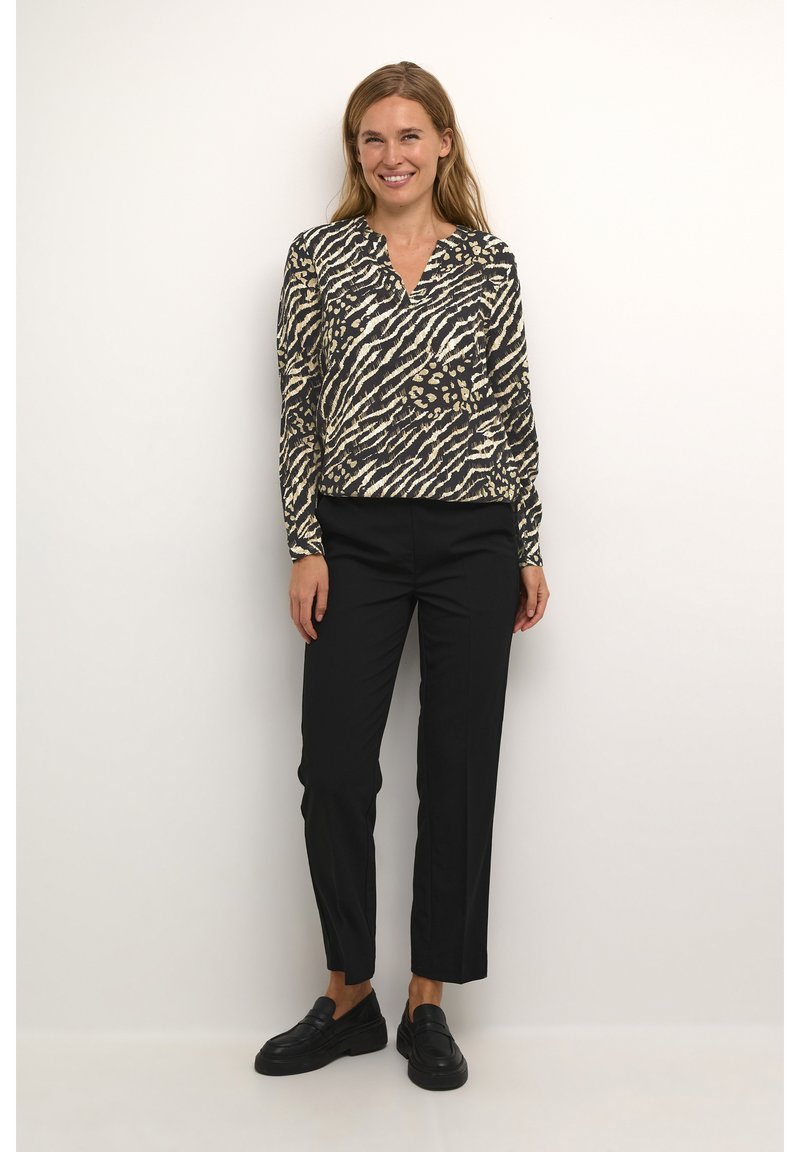 Zwart en beige blouse met lange mouwen met een zebra- en luipaardprint, gecombineerd met zwarte tapered broek en zwarte loafers.