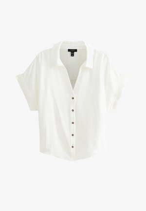 Blouse blanche à manches courtes avec col et manches retroussées, dotée de cinq boutons foncés sur le devant.