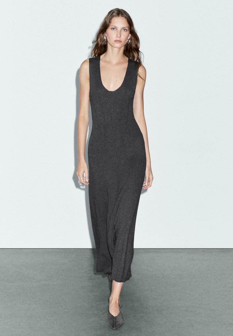 Robe en tricot grise avec un décolleté en V profond, sans manches et à coupe ample. Les textures élégantes de sa silhouette longue et fluide rehaussent son apparence générale.