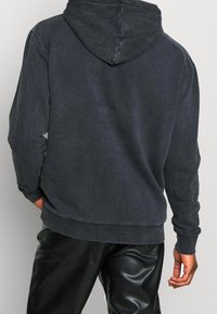 Sudadera con capucha de color gris oscuro, fabricada en un tejido suave, que presenta un corte relajado, puños y cintura de canalé, con una textura sutil.