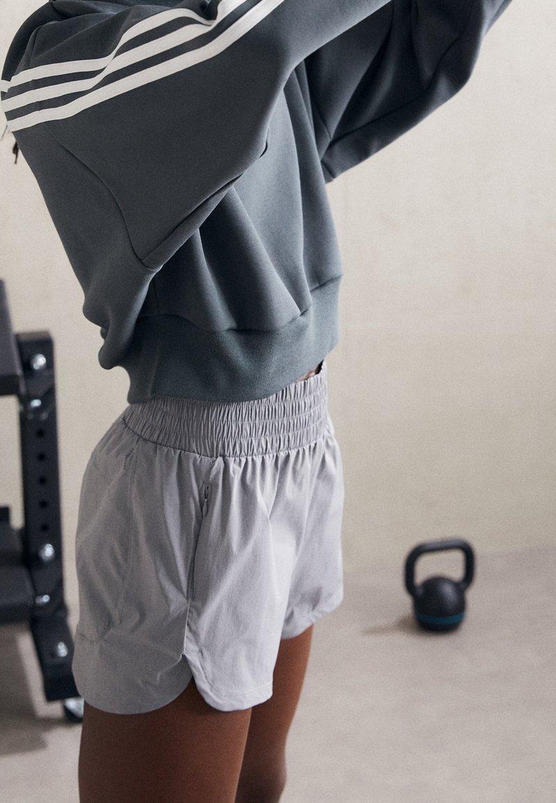 Grå sweatshirt med vita ränder på ärmarna, tillsammans med ljusgrå, elastiska idrottsshorts med sidoklyftor och fickor.