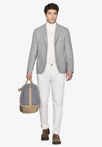 Grå houndstooth-mønstrede blazer over en hvid turtleneck, hvide bukser og brune sko. Bærer en grå og beige rygsæk.