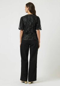 Zwarte top van bloemenkant met pofmouwen, gecombineerd met zwarte wijde jeans en beige plateauzolen. Gladde textuur en verfijnd bloemenpatroon.