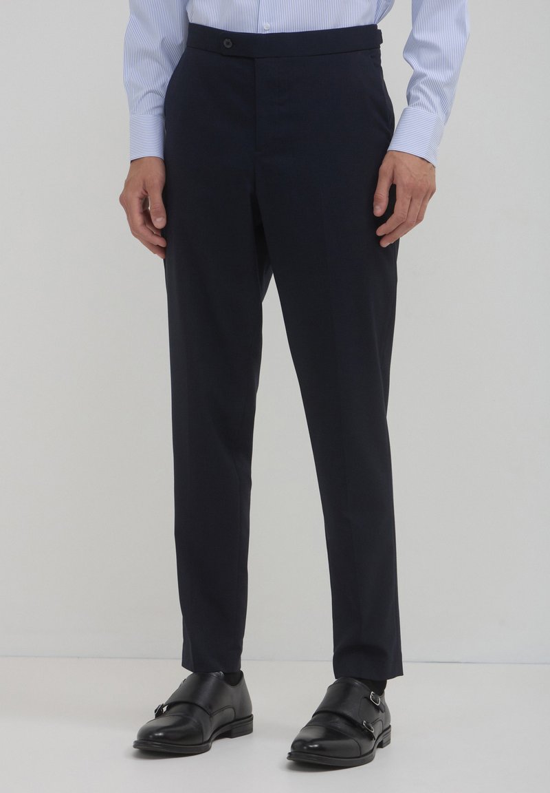 Marineblaue, taillierte Hosen mit schmaler Passform, aus glattem Stoff gefertigt, mit flachem Frontteil, seitlichen Taschen und einem dezenten Knopfverschluss.