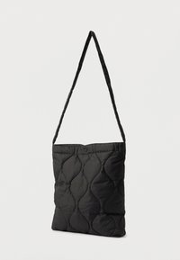 Saco tote acolchoado preto com um design plano, apresentando uma longa alça de ombro e um fecho de botão na parte superior. Textura suave e forma simples.