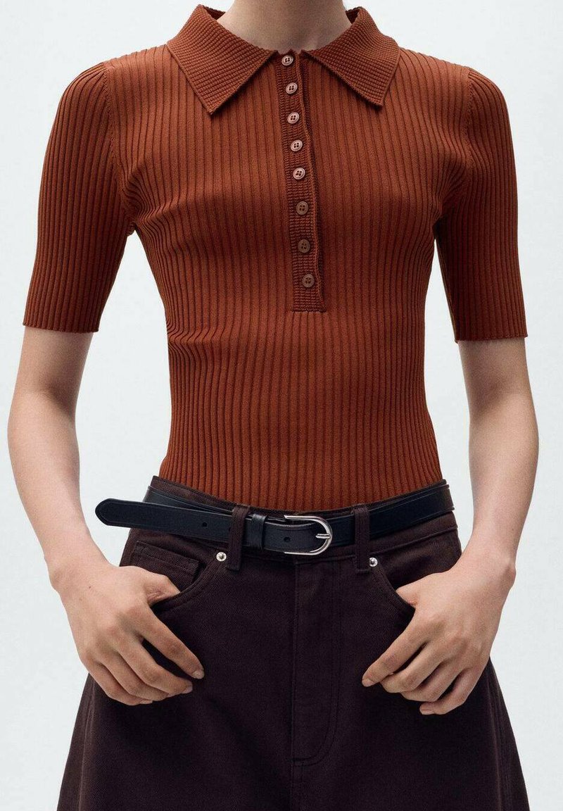 Polo à manches courtes côtelé en orange rouille avec une patte de boutonnage ; associé à un pantalon marron foncé et une ceinture noire.