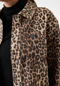 Läckerjacka i leopardmönster i beige och bruna toner, med silverfärgade tryckknappar och en synlig framsida ficka med en logotags.