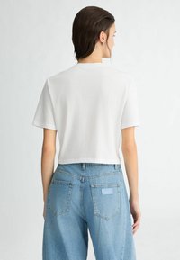 T-shirt blanc coupé avec des manches courtes, fabriqué en coton doux, associé à un jean bleu clair taille haute avec deux poches à l'arrière.