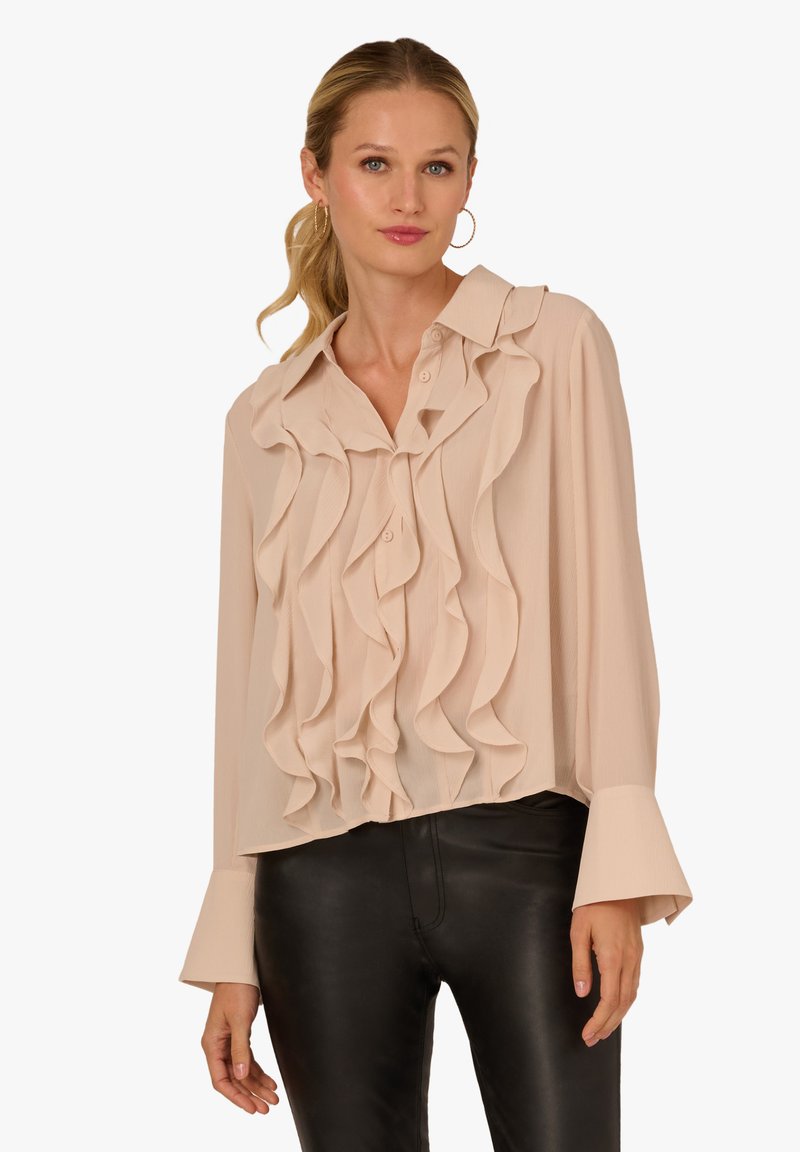 Beige blouse featuring ruffle detailing, a collared neckline, and long bell sleeves, paired with black fitted pants.