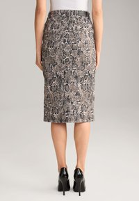 Jupe crayon avec un motif serpent dans des tons de beige et de noir, présentant une silhouette ajustée et une étiquette de marque visible à la taille.