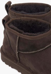 Brązowe zamszowe botki za kostkę z grubą czarną futrzaną wyściółką i detalami przeszyć wzdłuż krawędzi, wyposażone w pętelkę z tyłu.