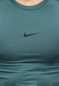 Κοντινό πλάνο άνω κορμού που φορά μια πράσινη αθλητική μπλούζα με το μαύρο λογότυπο Nike Swoosh στο κέντρο του στήθους.