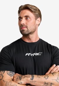 Svart atletisk T-shirt med korta ärmar och rund halsringning. Har en framträdande vit "RVRC" logotyp på framsidan. Slät textur.