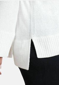 Maglione bianco lavorato a maglia con orlo a coste e spacchi laterali, caratterizzato da una finitura testurizzata e un tessuto morbido, abbinato a pantaloni neri.