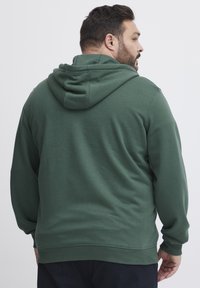 Felpa verde realizzata in tessuto morbido. Presenta un cappuccio con cordino e polsini a costine. Design semplice senza fantasie o loghi.