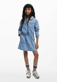 Denimkleit heleda helesinise tooni, pikkade varrukatega, tõmbluku sulgemisega, elastse vöökoha, küljetaskute ja peene mustriga; koos triibuliste sokkide ja tossudega.