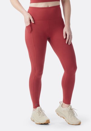 Rote Sportleggings mit hohem Bund, Seitentasche, glattem Material und kontrastierenden Abschlüssen. Kombiniert mit hellen Sportschuhen.