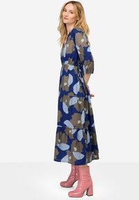 Vestido maxi azul con estampados florales, cuenta con mangas tres cuartos, una cintura ajustada y una falda en capas. Un par de botas de tacón altas rosas.