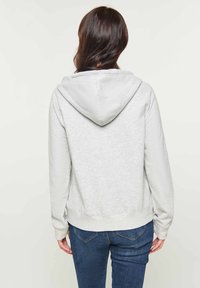Felpa grigia con cappuccio, dal taglio morbido, con polsini e orlo a costine, mostrata da dietro. Indossata con jeans blu scuro.