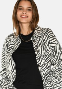 Zebraprint denimhijakki, jossa on kauluksen pääntie, napit ja sivutaskut, yhdistettynä mustaan T-paitaan ja kultaketjuun.
