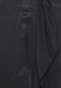 Tissu noir avec une texture lisse et légèrement côtelée, présentant un accent drapé qui cascade le long d'un côté.