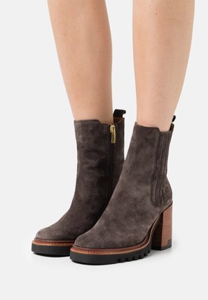 Bottines en suede gris avec un talon carré, fermeture éclair sur le côté et panneaux élastiques ; surface texturée et détails de couture autour de la semelle.