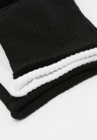 Pila di calze a coste nei colori bianco e nero piegate su una superficie bianca, che mette in risalto la texture e i bordi.