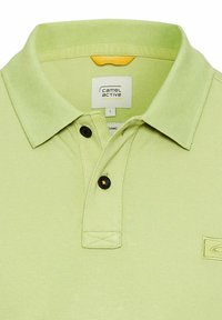 Lichtgroene polo gemaakt van biologisch katoen, met een ribbelkraag, een knoopsluiting met twee knopen in het zwart, en een klein logodetail.