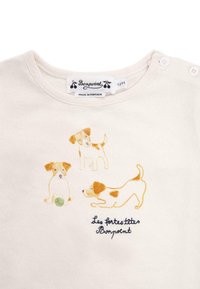 Jasna kremowa koszulka z lekkiego materiału, ozdobiona trzema haftowanymi psami w kolorze żółtym i brązowym. Zawiera metkę z napisem "Bonpoint" oraz dwa zapięcia na guziki na ramieniu.