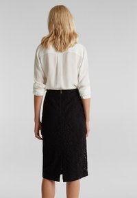 Gonna di pizzo nero con spacco sul retro, abbinata a una camicia bianca con maniche arrotolate, realizzata in tessuto morbido e leggero.