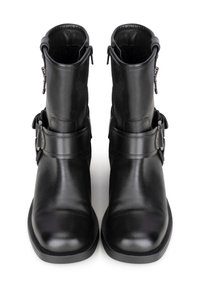 Botines de cuero negro con puntera redonda, cierres de cremallera y correas decorativas. Textura suave y suelas sólidas y resistentes.