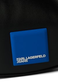 Juodas tekstūruotas audinys su mėlynu label, kuriame užrašyta "KARL LAGERFELD JEANS" balta spalva. Dizainas yra stačiakampio formos su lygiomis kraštinėmis.