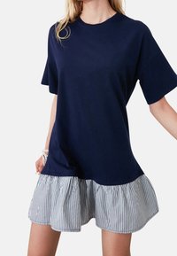Navy T-Shirt-Kleid mit kurzen Ärmeln, das einen gestreiften Rüschensaum hat. Weiches Baumwollmaterial mit lockerer Passform und rundem Ausschnitt.