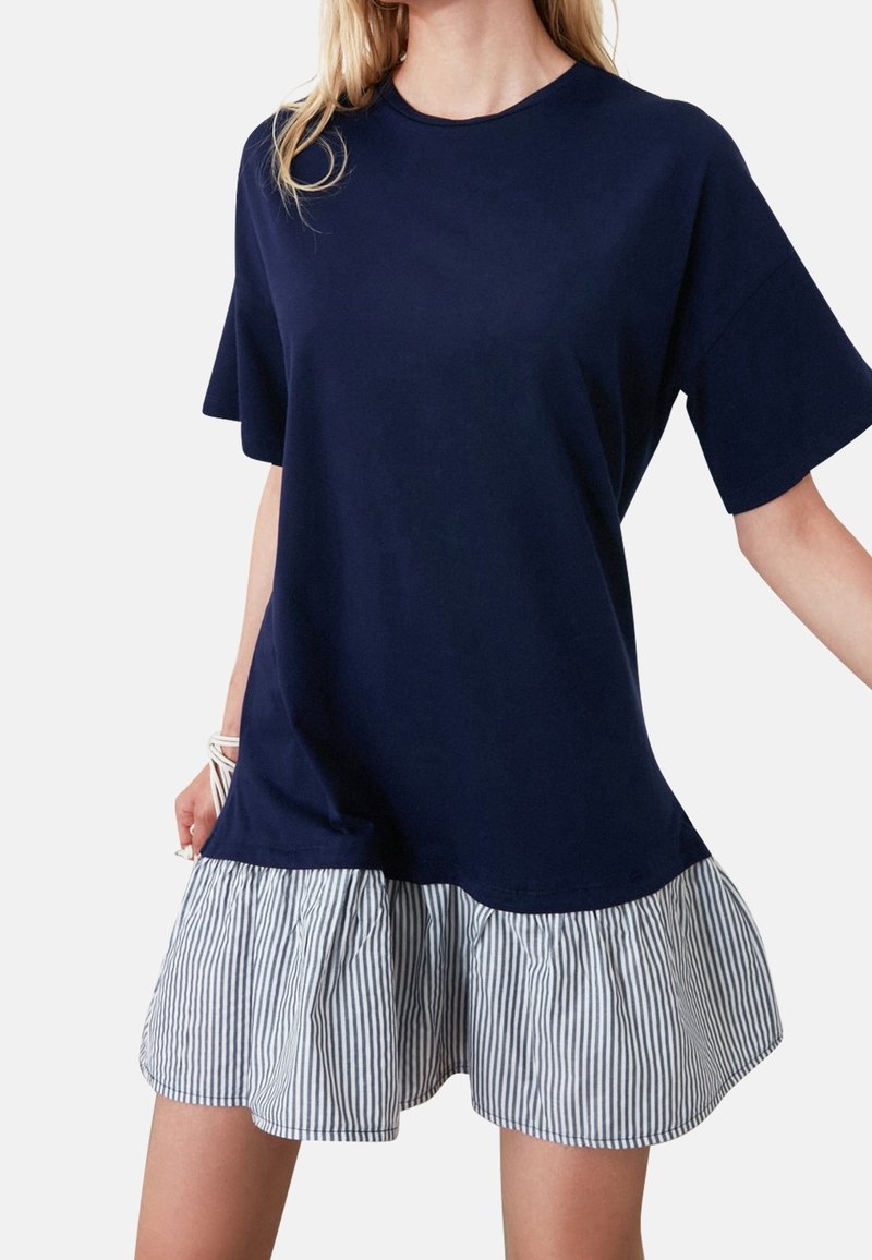 Navy T-Shirt-Kleid mit kurzen Ärmeln, das einen gestreiften Rüschensaum hat. Weiches Baumwollmaterial mit lockerer Passform und rundem Ausschnitt.
