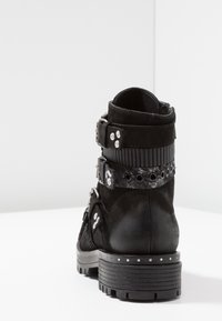 Botas negras hasta el tobillo con parte superior de ante texturizado, hebillas decorativas, tachuelas plateadas y suela de goma resistente. Presenta un diseño en capas.