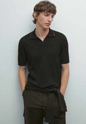 Kortærmet sort ribbet polo-shirt med en subtil brun detalje på kraven, parret med mørke bukser, der har et bundet stofdetalje i taljen.