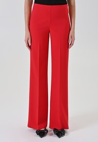 Pantaloni rossi a gamba larga con texture liscia, vita alta e vestibilità su misura. Abbinati a scarpe nere con dettagli a fiocco.