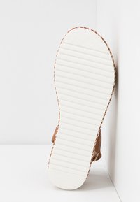 Semelle de sandale vue de face avec dessous texturé blanc et bord tressé marron, sur fond blanc aux coins marqués.