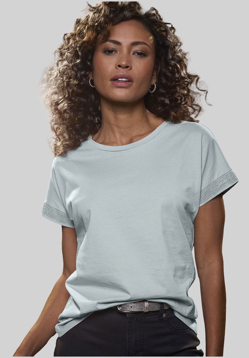 Light blue cotton t-shirt with short rolled sleeves featuring a textured pattern on the cuffs. Worn with dark pants and a metallic belt.