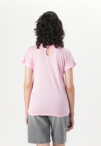 Short-sleeved, pink T-shirt with a round neckline and a keyhole detail at the back. Paired with gray shorts. Soft fabric, casual fit.