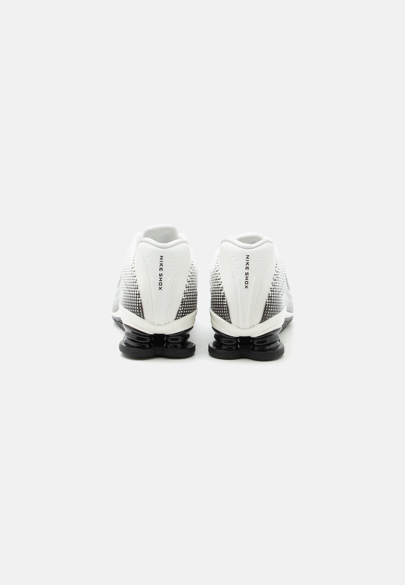 Par de zapatillas Nike Shox blancas y negras vistas desde atrás, destacando el diseño distintivo del tacón con resortes apilados.