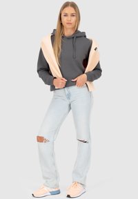 Grijze hoodie met een trekkoord, gecombineerd met lichtblauwe gescheurde jeans. Draagt perzikkleurige sneakers met blauwe accenten. Neutrale achtergrond.